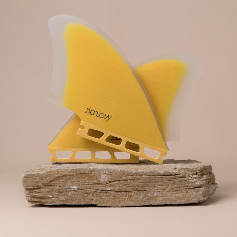 Pair of Deflow Palm twin fins in mustard color on a stone base.