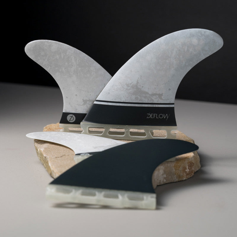 Deflow SUPRA QUATTRO L single tab shortboard fins displayed on a stone.